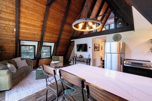 A spacious loft with a high ceiling, wooden beams, a large dining table, and a kitchen area. - Secluded A-Frame on 10 Acres | At the Pines (Fennville)