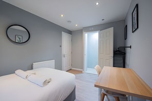 Une chambre à coucher avec un lit, une table en bois, un radiateur et une porte donnant sur une autre pièce.