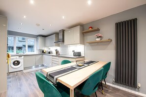 Cozinha moderna com máquina de lavar embutida, área de jantar com mesa e cadeiras, e vista para o exterior.