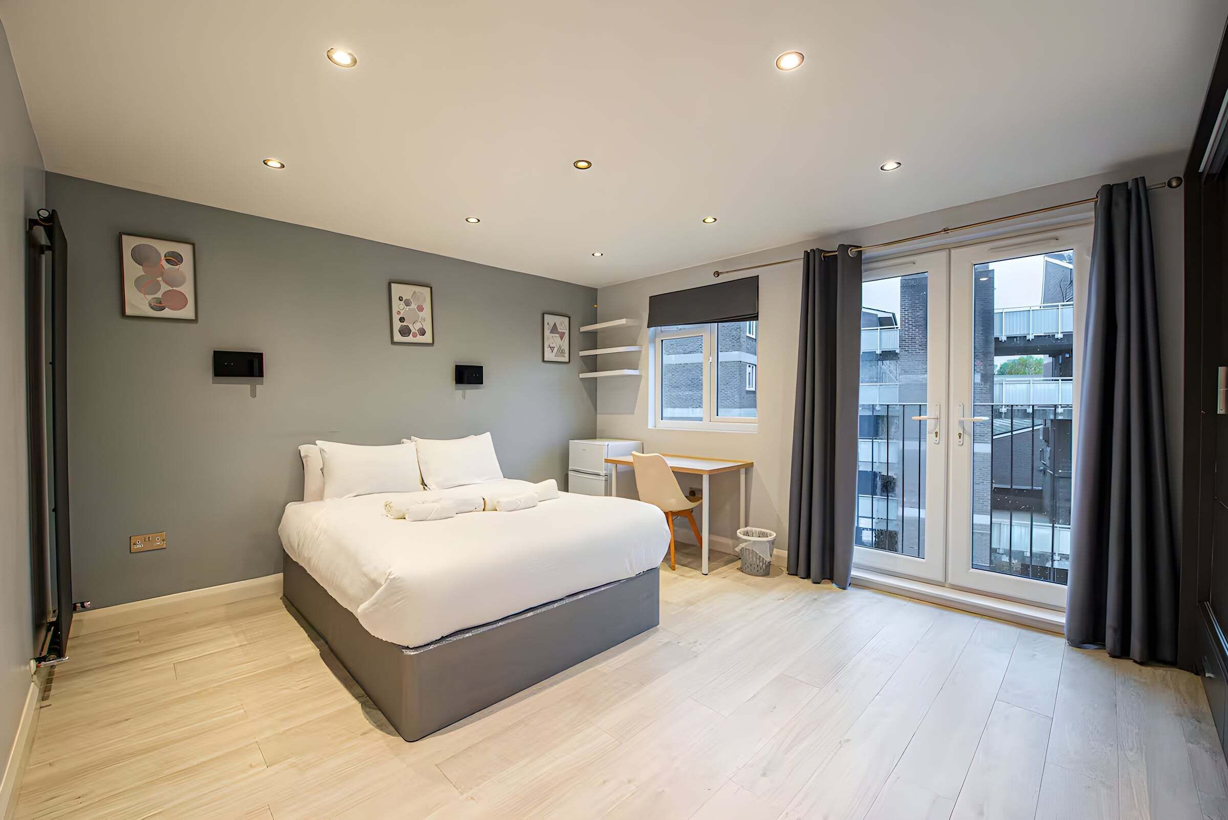 A modern bedroom with a bed, a desk, and a large window.