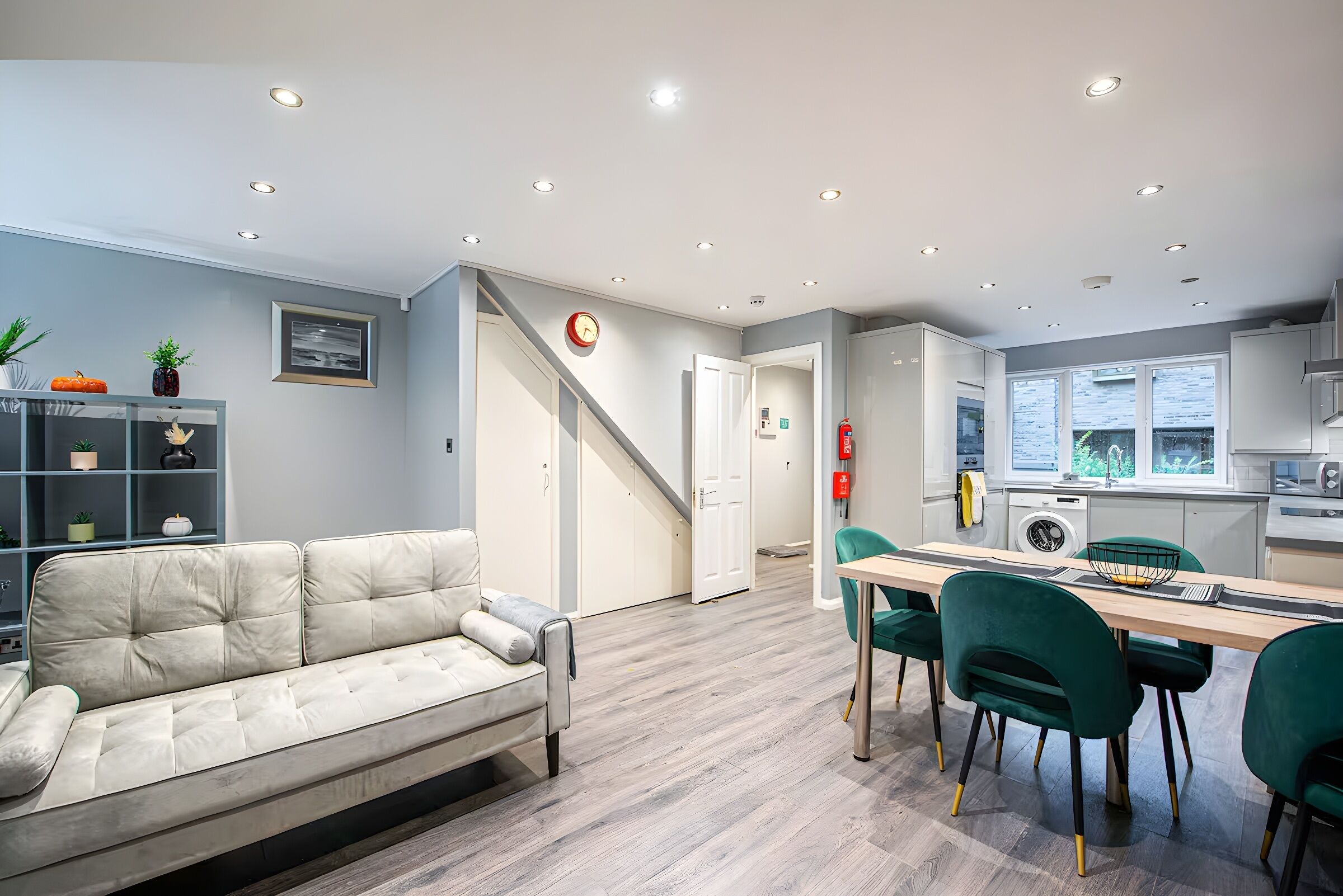 Ein modernes Wohnzimmer mit einer Couch, einem Essbereich mit Tisch und Stühlen, einer Küche mit Geräten und einer Treppe, die zu einer weiteren Ebene führt.