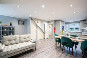 A modern living room with a sofa, a dining area with a table and chairs, a kitchen with appliances, and a staircase leading to another level. - Luxury 4BR House|Contractors • Corporate •Jacuzzi (London)