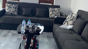 Un salon avec un canapé, deux fenêtres, un luminaire au plafond et une table sur laquelle se trouvent des bouteilles.