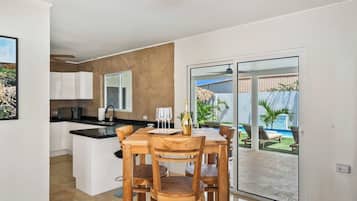 Eine moderne Küche mit Kochinsel, Essbereich mit Holzkästen und Blick auf einen Swimmingpool durch eine Glastür.
