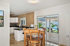 Una cocina moderna con una isla central, una zona de comedor con sillas de madera y vista a una piscina a través de un ventanal.