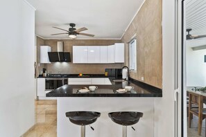 Una cocina moderna con una isla central, ventilador de techo y paneles de madera en las paredes.