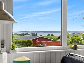 A room with a large window overlooking a body of water, a red building, and greenery. - "Agla" - 350m from the sea by Interhome (Aabenraa)