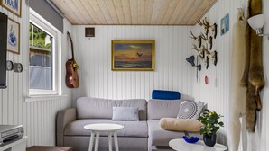 Tunnelmallinen olohuone, jossa on sohva, kaksi pientä pöytää, kitara sekä erilaisia seinäkoristeita, kuten maalaus ja eläinten kallot.