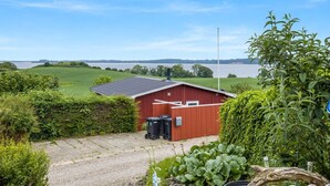 Punainen rakennus, jossa on kalteva katto, sorapäällysteinen ajotie ja näkymä suurelle vesistölle.