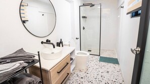 Een moderne badkamer met een ronde spiegel, een wastafel, toilet en een douchecabine van glas.