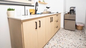 Een keuken met houten kastjes, een aanrecht, een koffiezetapparaat en een prullenbak.