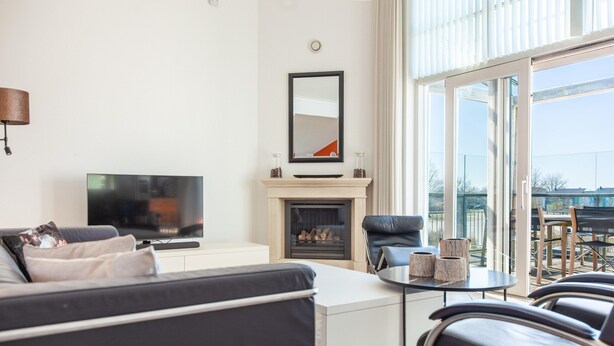 A modern living room with a flat-screen TV, a fireplace, a sofa, and a dining area with chairs. - Luxury Makkum Beachvilla for 6 (Makkum)