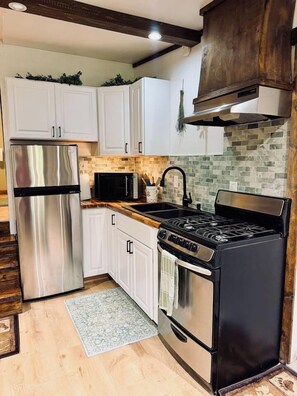 A kitchen with white cabinets, a stainless steel refrigerator, a black stove, and a tiled backsplash.