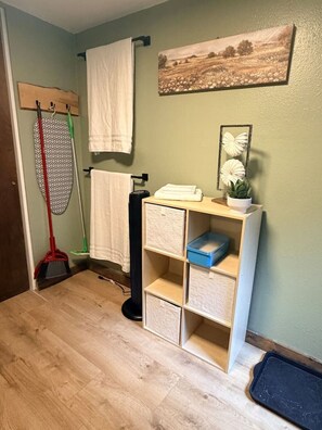 Ein Badezimmer mit Holzboden, einem Handtuchhalter, einem Regal mit Aufbewahrungsboxen und einem Bild an der Wand.