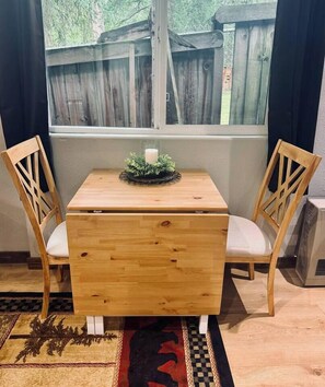 A wooden table with two chairs, a small decorative item on the table, and a window with a view of a wooden fence.