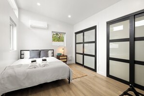 Quarto moderno com cama, mesa de cabeceira, abajur e vista para um jardim pela janela.