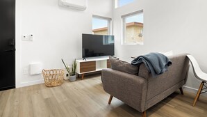 A modern living room with a flat-screen TV, a grey sofa, a wicker basket, and a potted plant. - Spacious w/1BR 1Bath - Near DTLA (Los Angeles)