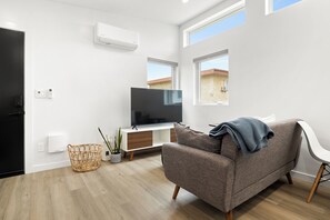 Uma sala de estar moderna com uma televisão de tela plana, um sofá cinza, um cesto de vime e um vaso de plantas.