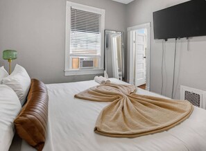 Habitación de hotel con cama, espejo, televisor y ventana con persianas.