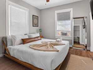A bedroom with a bed, two windows with blinds, a bedside table with a lamp, and a mirror on the wall. - Downtown CO Springs 1BR Cottage with Sunroom (Colorado Springs)
