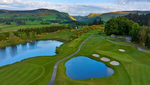 A golf course with a pond, green hills, and a clear sky. - Lochside Perthshire Lodge for 4 (Auchterarder)