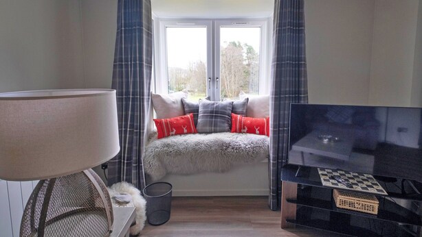 A bedroom with a bed, a TV, a window with curtains, and a lamp. - Lochside Perthshire Lodge for 4 (Auchterarder)