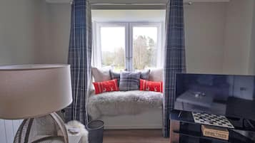 A bedroom with a bed, a TV, a window with curtains, and a lamp.