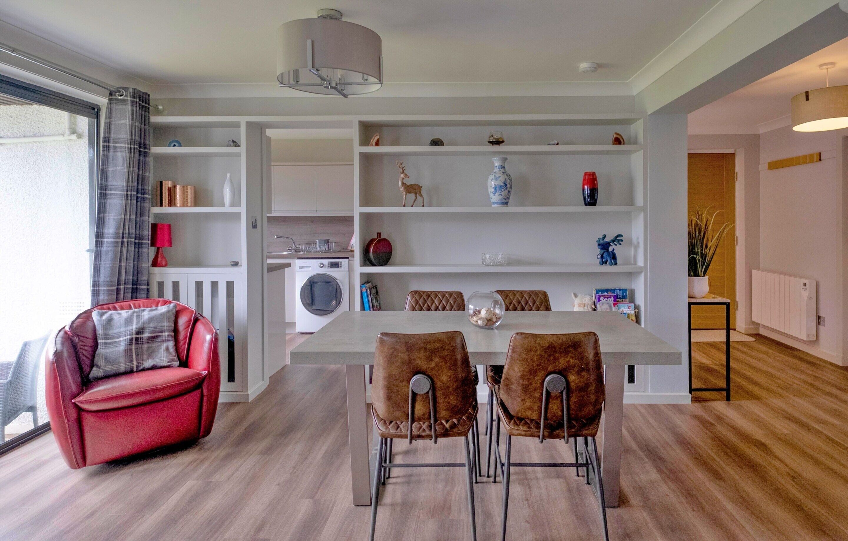 A modern kitchen with a dining area, a red sofa, and a large window with curtains.