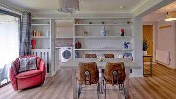 A modern kitchen with a dining area, a red sofa, and a large window with curtains.