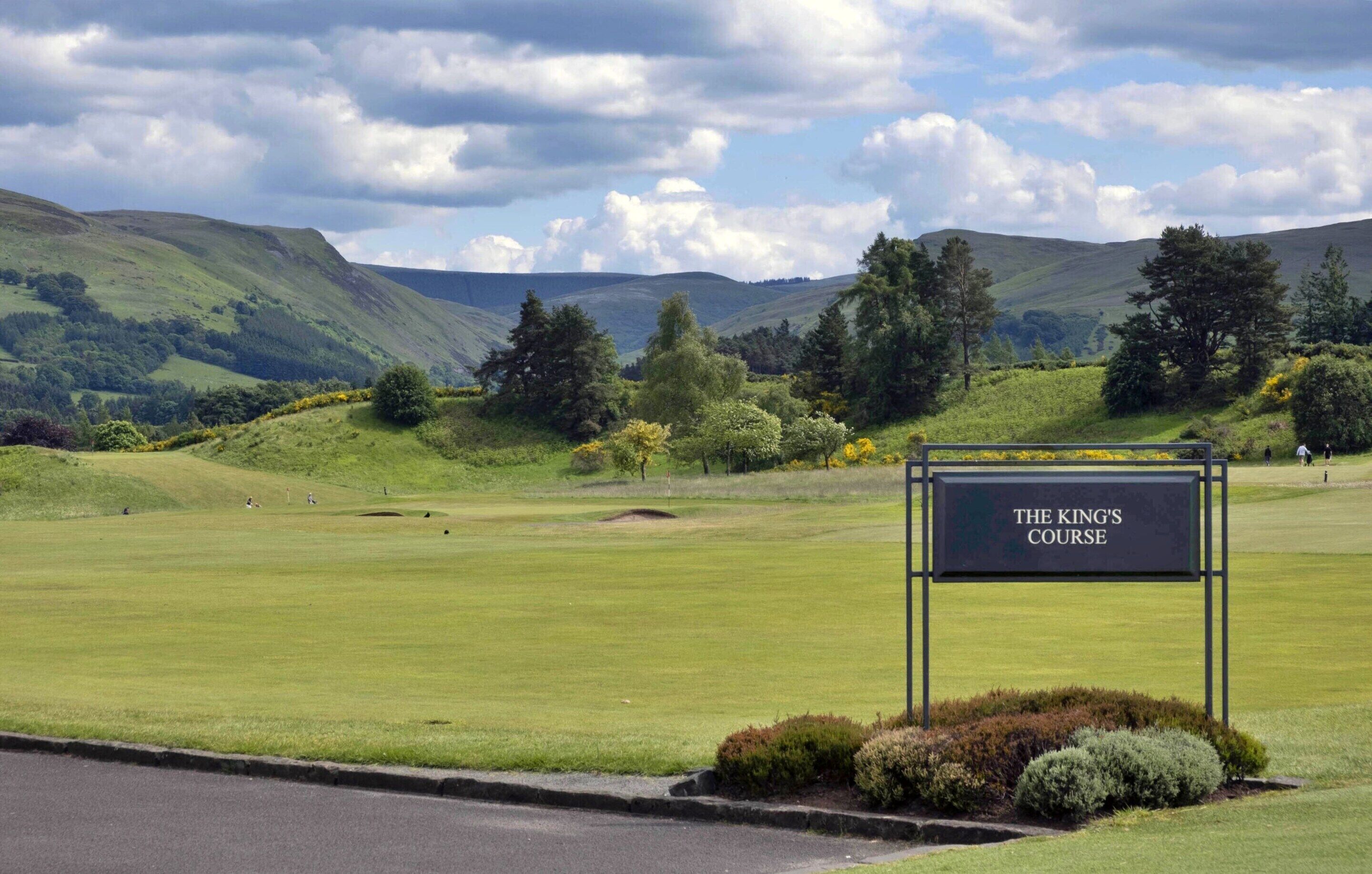 A sign for The King's Course, a golf course with a view of rolling hills and trees.