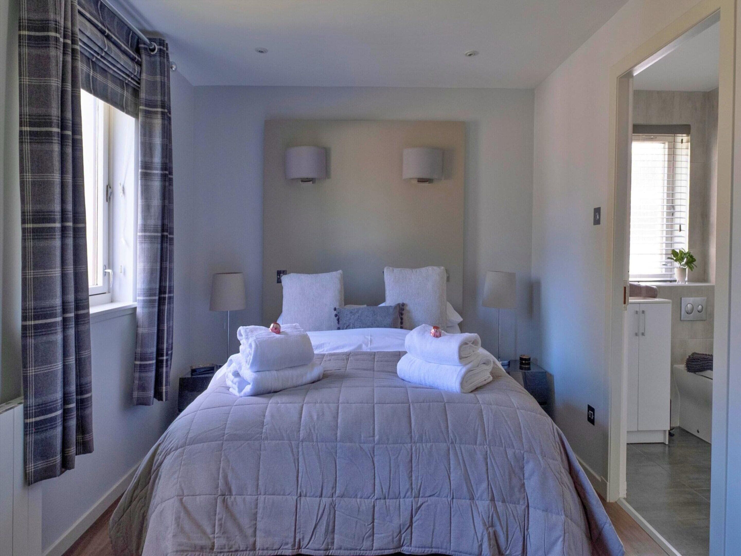 Habitación de hotel con una cama grande, dos lámparas de noche, una ventana con cortinas y vistas al baño.