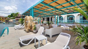 A covered outdoor seating area with lounge chairs and tables, overlooking a body of water with boats. - Casa Astral  (Flores)