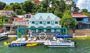 Una propiedad frente al mar con una casa grande, un espacio de estar al aire libre cubierto y varios barcos.