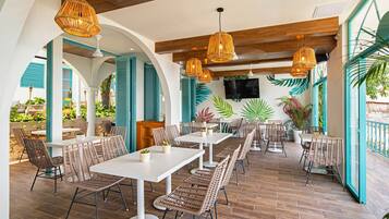 Een restaurant met rieten meubels, witte tafels en hangende rieten lampen.