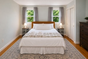A neatly arranged bedroom with a large bed, two bedside tables with lamps, a dresser, and a view of greenery outside. - Spacious Upstairs Apartment Near Stowe Mountain (Stowe)