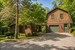 A wooden cabin with a gravel driveway, surrounded by trees and greenery. - Spacious Upstairs Apartment Near Stowe Mountain (Stowe)