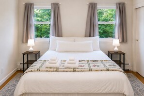 A bedroom with a bed, two bedside tables, a window with curtains, and a view of greenery outside. - Spacious Upstairs Apartment Near Stowe Mountain (Stowe)