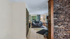 Un couloir mène à un salon doté d’un mur en pierre, d’un canapé, d’une lampe et d’un tapis.