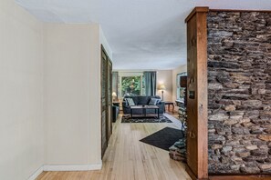 Ein Flur, der in ein Wohnzimmer mit Steinwand, Sofa, Lampe und Teppich führt.