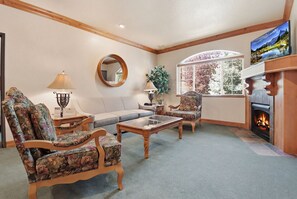 Ein Wohnzimmer mit Kamin, floral gemusterten Sesseln, einer Couch und einem großen Fenster mit Blick.
