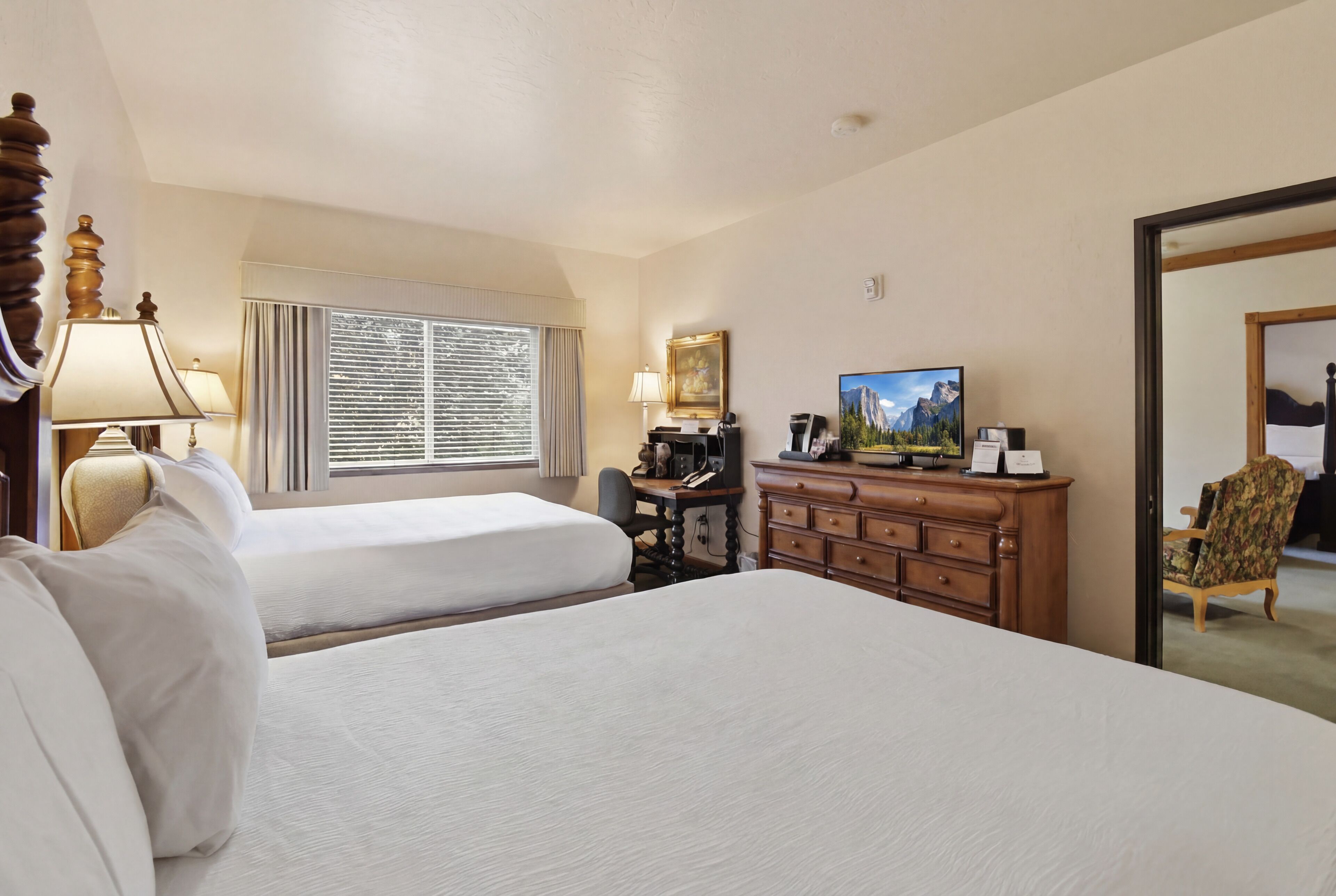 A hotel room with two beds, a desk with a computer, a television, and a mirror.