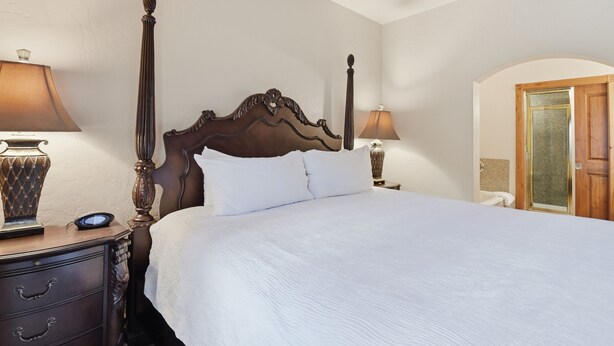 A hotel room with a four-poster bed, a nightstand with a lamp, and a wooden door. - Villa 2080 1 Bed 1 Bath Full Kitchen in the heart of Midway Utah (Midway)