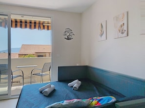 A hotel room with a bed, a small table, a chair, and a balcony with a view of buildings. - Les Aigues Marines by Interhome (Saint Cyr sur Mer La Madrague)