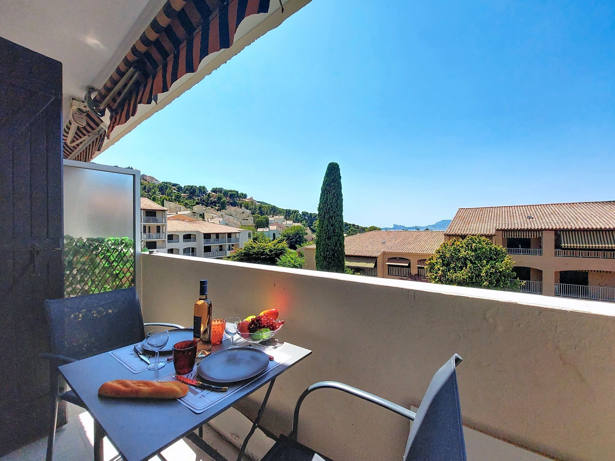 A balcony with a table set for two, a bottle, and a bowl of fruit.