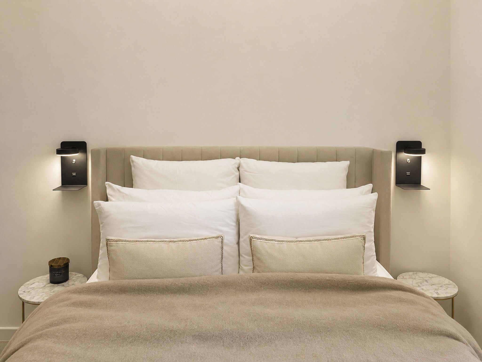 A bed with a beige headboard, two bedside tables, and wall-mounted nightstands.