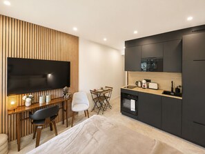 Een moderne kitchenette met een flatscreentelevisie, een zithoek met een tafel en stoelen, en een bank.