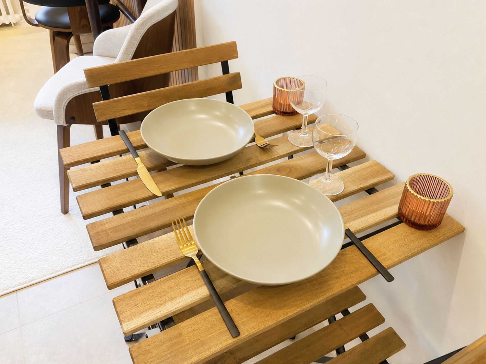 Une table à manger avec deux assiettes, des fourchettes et des verres à vin, posée sur un banc en bois.