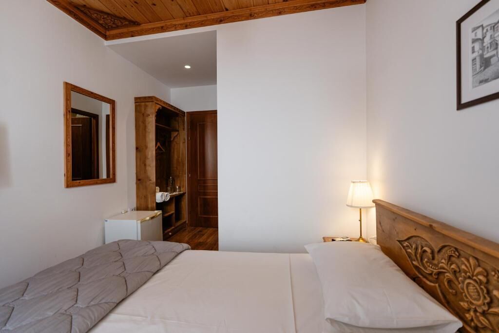 A bedroom with a bed, bedside table, lamp, wardrobe, and a mirror.