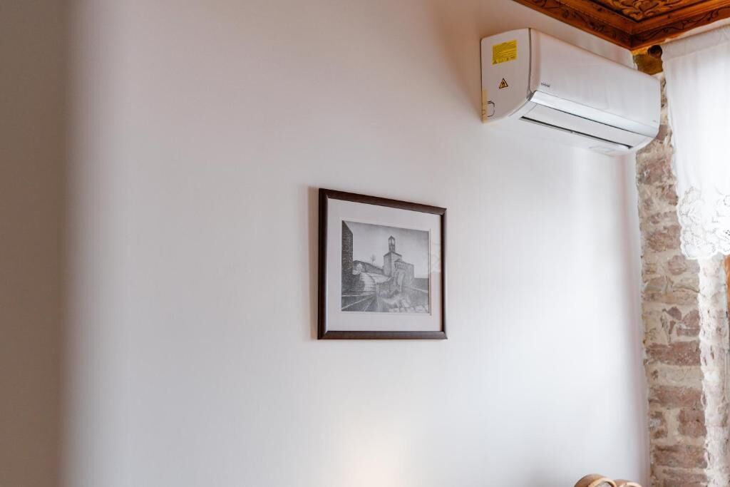 Um quarto com uma fotografia a preto e branco emoldurada na parede, um aparelho de ar condicionado branco fixado na parede e teto de madeira.