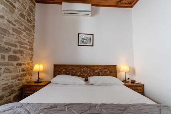 A bedroom with a bed, two bedside lamps, a framed picture on the wall, and a stone wall on one side. - 4 Rooms Boutique (Gjirokastër)
